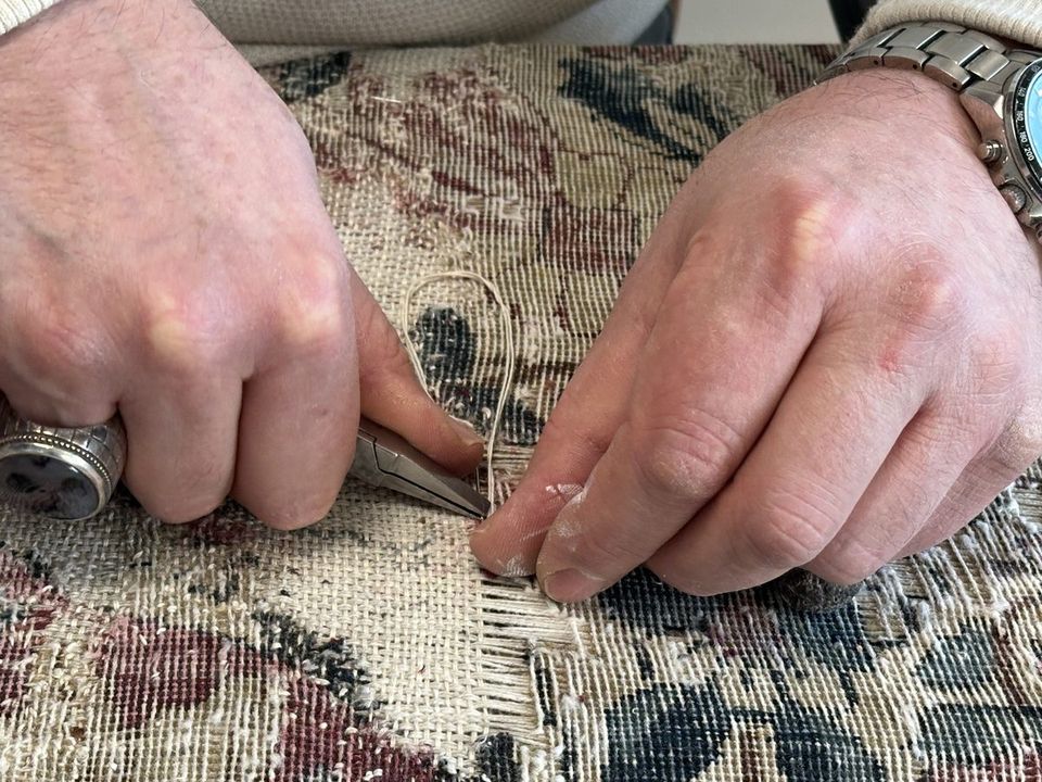 Mains d'artisan reconstituant les fils de chaîne d'une zone usée, à la pince