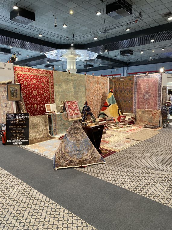 Le stand de La Maison de la Perse sur un salon : tapis persans suspendus, tapis en soie et objets d'art