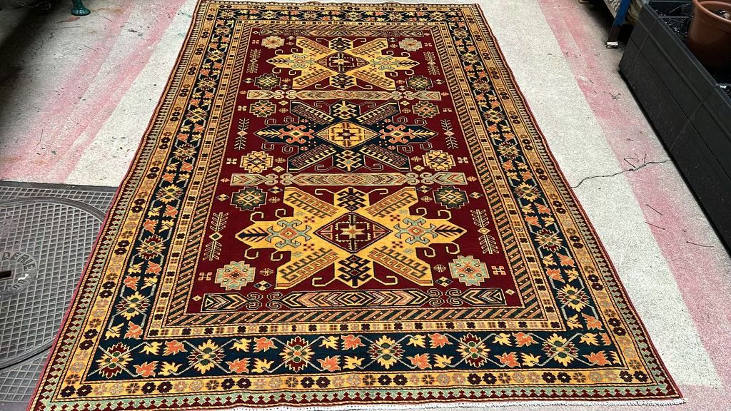 Tapis Kazak noué main : grands médaillons étoilés jaunes sur champ rouge, bordure bleu nuit