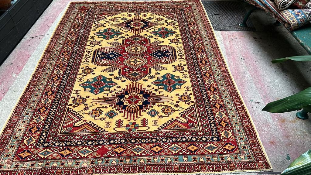 Tapis Kazak noué main à champ jaune, médaillons géométriques rouges, bleus et verts, large bordure rouge