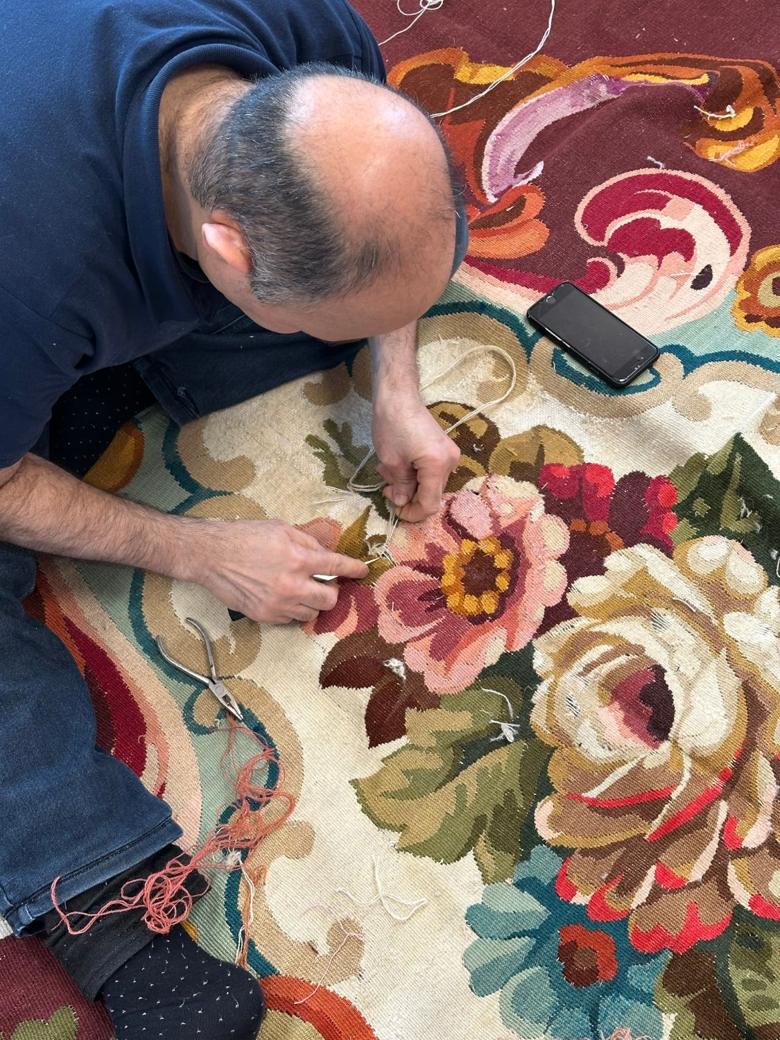 Un artisan de La Maison de la Perse restaure à la main un tapis à motifs floraux